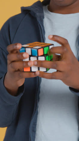 Vertical-Video-Studio-Close-Up-Of-Young-Boy-On-ASD-Spectrum-Solving-Puzzle-Cube-On-Yellow-Background